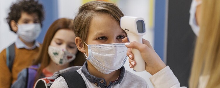 Female-teacher-with-medical-mask-checking-student-s-temperature-in-school